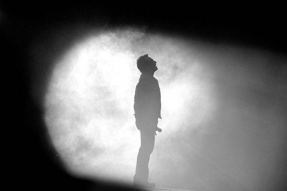 Bono in silhouette under a stage spotlight