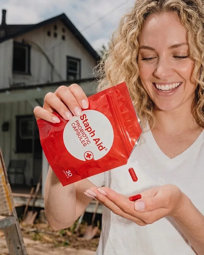 Smiling woman pouring a Staph Aid capsule from the pouch into her palm